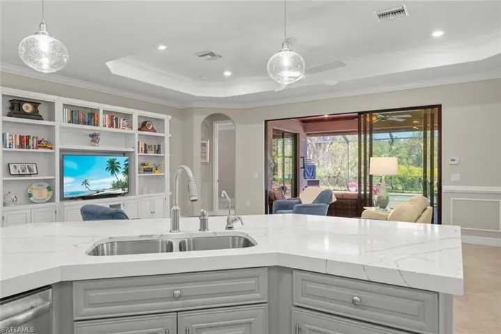 Kitchen island with stainless steel sink and gooseneck faucet, quartz countertops, gray cabinetry, and pendent lights.
