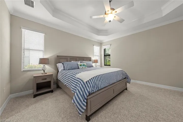Primary bedroom with tray ceiling with crown molding and ceiling fan