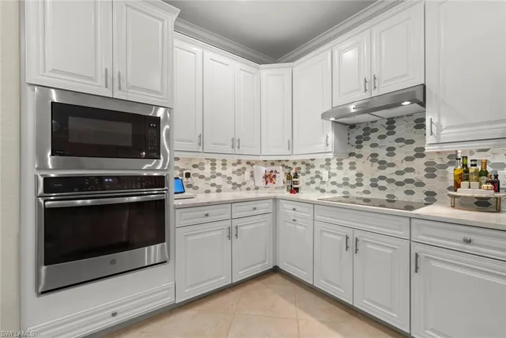 White cabinetry, stainless steel built-in oven and microwave, induction cooktop, light-toned quartz countertop, mosaic tile backsplash