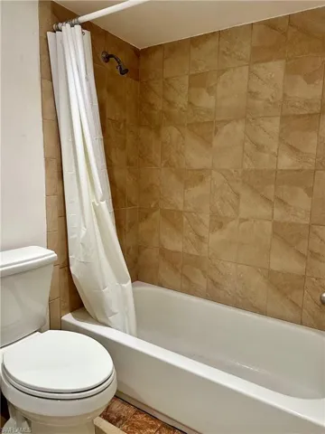 Bathroom featuring toilet and shower / bathtub combination with curtain