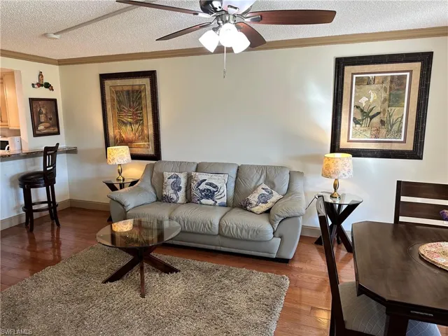 Living room with a textured ceiling, crown molding, hardwood / wood-style flooring, and ceiling fan