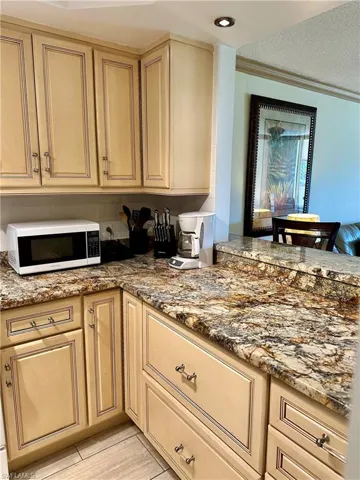 Kitchen with light stone counters, cream cabinetry, ornamental molding, and a textured ceiling