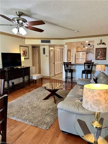 Living area featuring crown molding, light wood-style floors, ceiling fan, and a textured ceiling