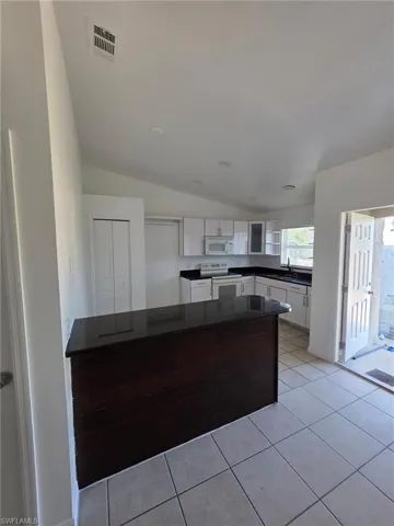 Kitchen featuring white cabinetry, white appliances, light tile patterned floors, dark countertops, and vaulted ceiling