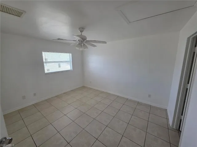 Empty room with light tile patterned floors, ceiling fan, and attic access
