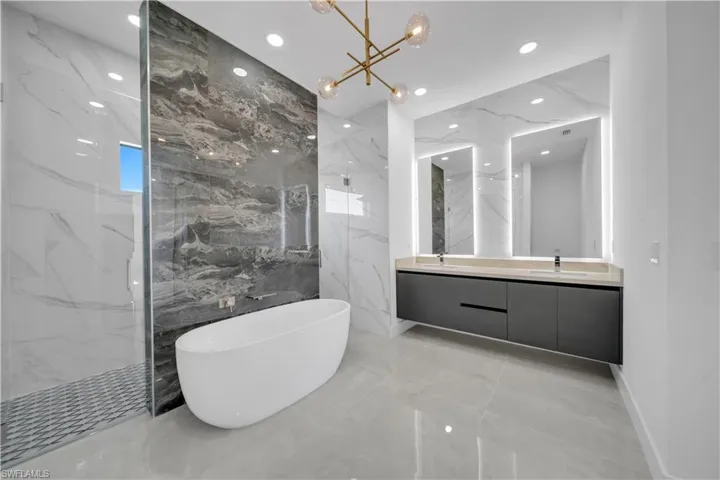 Bathroom with marble tiled floors, double vanity, a soaking tub, a marble finish shower, and stone wall