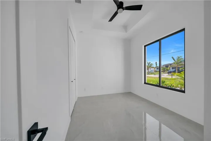Empty room with light marble finish flooring, a ceiling fan, and a raised ceiling