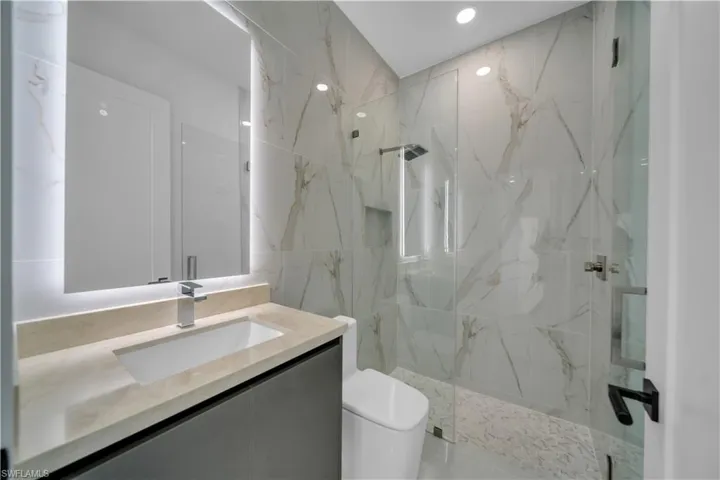 Full bathroom with a marble finish shower, toilet, vanity, and recessed lighting