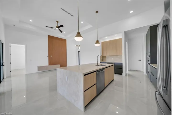 Kitchen with modern cabinets, stainless steel appliances, a raised ceiling, ceiling fan, and a sink