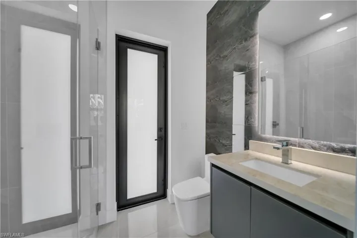 Bathroom with a stall shower, vanity, toilet, tile walls, and recessed lighting