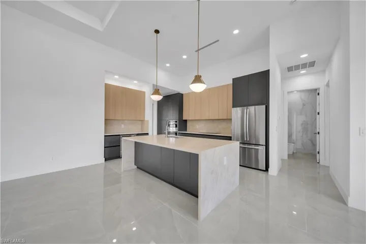 Kitchen featuring modern cabinets, freestanding refrigerator, light countertops, light marble finish flooring, and recessed lighting