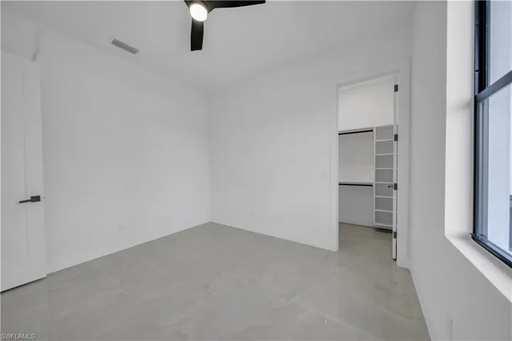 Unfurnished bedroom with a spacious closet, ceiling fan, marble finish floors, a closet, and baseboards