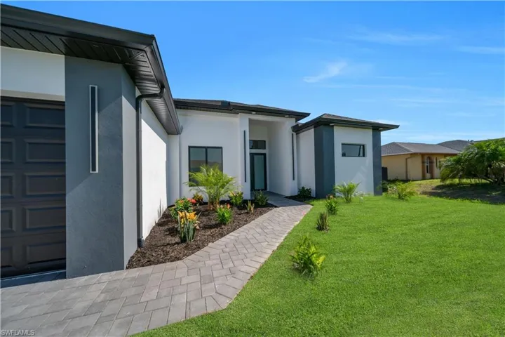 View of exterior entry featuring stucco siding, a lawn, and an attached garage
