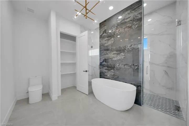 Full bath with a soaking tub, a marble finish shower, a chandelier, toilet, and marble tiled floors