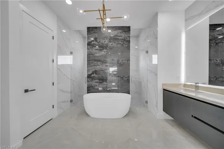 Bathroom with a marble finish shower, a freestanding bath, vanity, marble finish floors, and tile walls