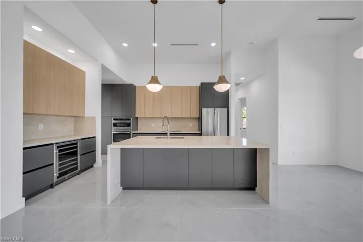 Kitchen with wine cooler, modern cabinets, appliances with stainless steel finishes, light countertops, and decorative backsplash