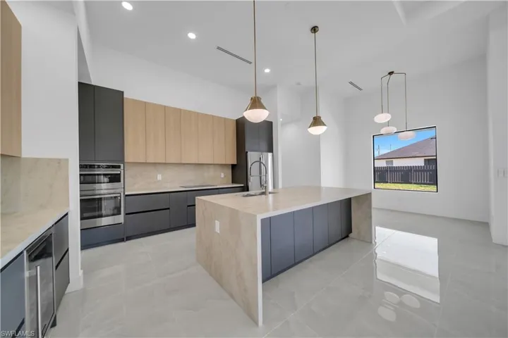 Kitchen with modern cabinets, stainless steel appliances, decorative backsplash, a center island with sink, and recessed lighting