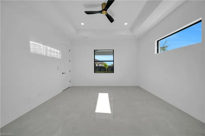 Unfurnished room with healthy amount of natural light, ceiling fan, recessed lighting, a raised ceiling, and light marble finish flooring