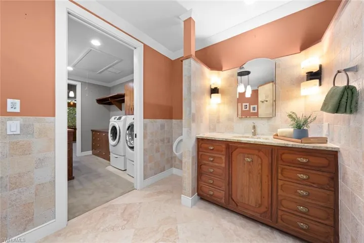 Bathroom featuring tile walls, vanity, washing machine and dryer, wainscoting, and crown molding