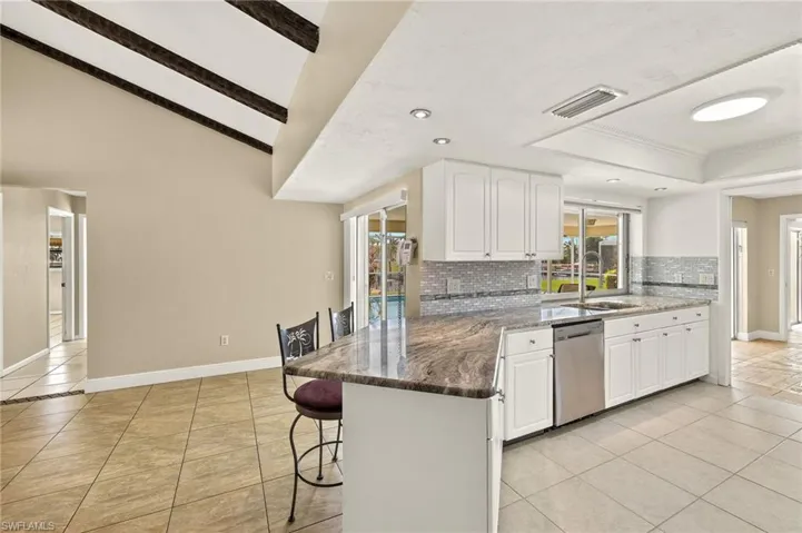 Kitchen featuring dark stone counters, a kitchen breakfast bar, light tile patterned floors, recessed lighting, and beamed ceiling