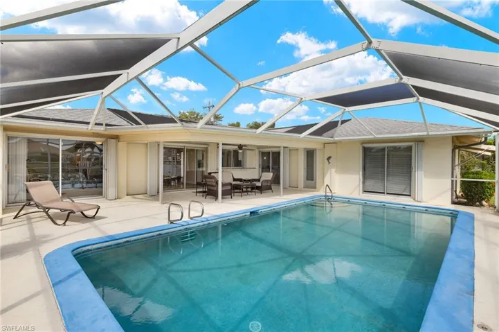 Rear view of house with a sunroom, a patio, an outdoor pool, and roof with shingles