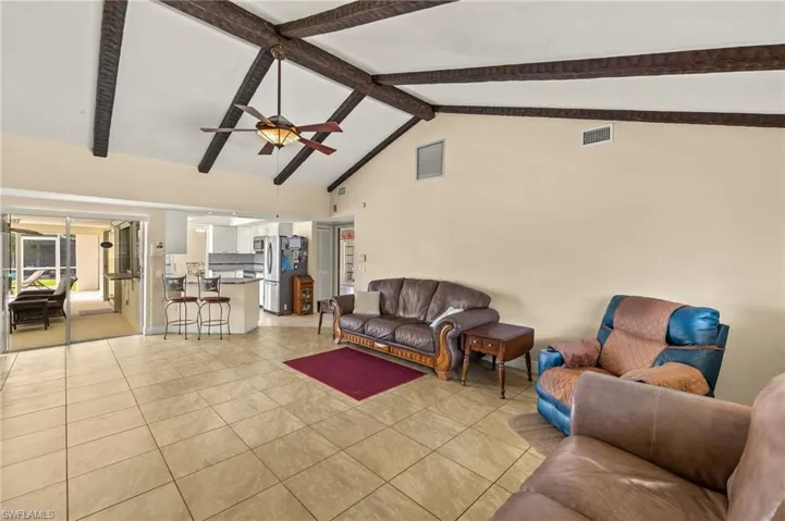 Living room with light tile patterned flooring, high vaulted ceiling, beamed ceiling, and ceiling fan