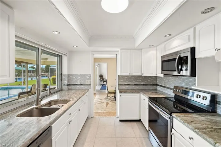 Kitchen featuring stainless steel appliances, a tray ceiling, white cabinets, light tile patterned floors, and crown molding