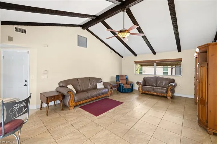 Living area featuring high vaulted ceiling, beam ceiling, light tile patterned floors, and ceiling fan