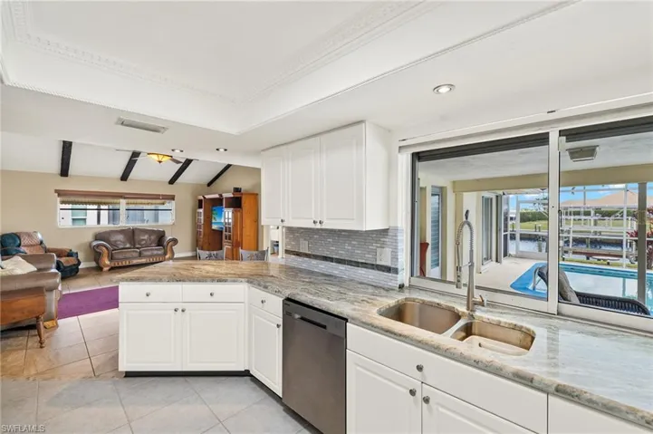 Kitchen featuring healthy amount of natural light, open floor plan, stainless steel dishwasher, and white cabinetry