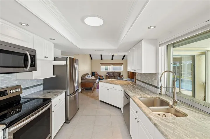 Kitchen with stainless steel appliances, backsplash, light stone counters, ornamental molding, and white cabinets