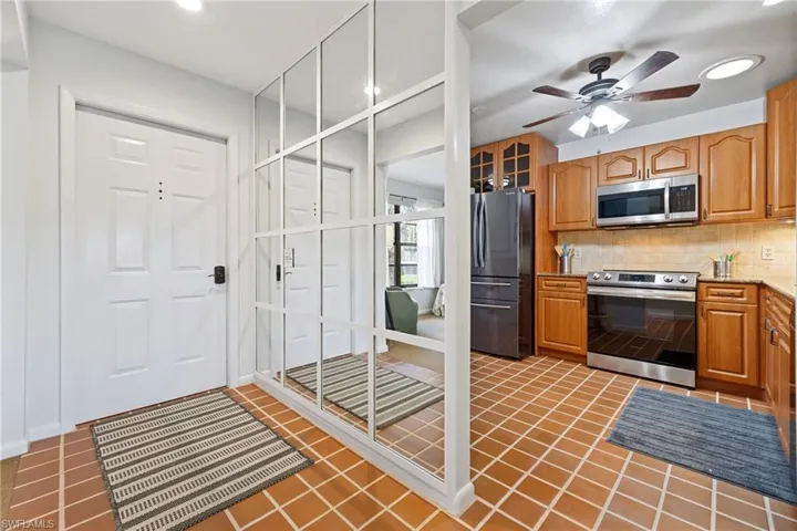 Kitchen featuring decorative backsplash, stainless steel appliances, brown cabinetry, dark tile patterned floors, and recessed lighting