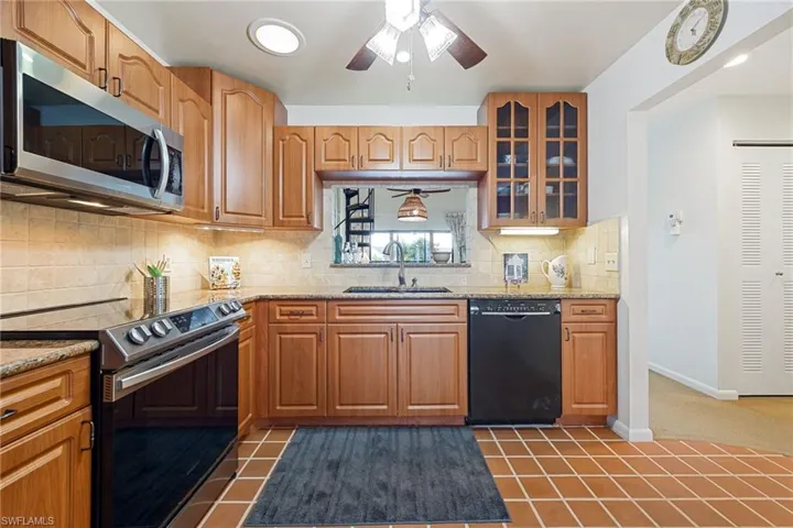 Kitchen featuring stainless steel appliances, ceiling fan, glass insert cabinets, tasteful backsplash, and light stone counters