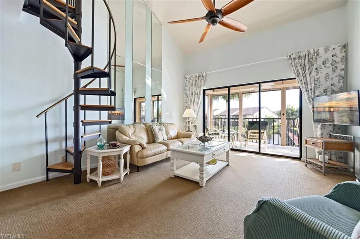 Living area featuring carpet, a towering ceiling, ceiling fan, and stairway