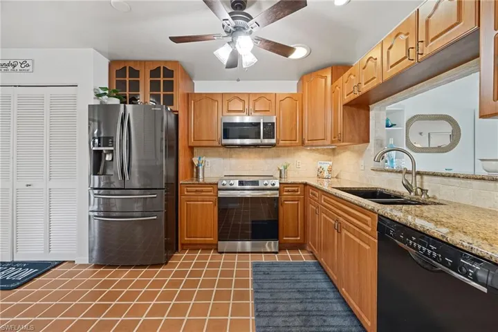 Kitchen featuring stainless steel appliances, light tile patterned flooring, decorative backsplash, light stone counters, and glass insert cabinets