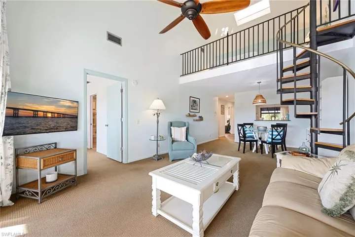 Living area with stairs, a ceiling fan, carpet flooring, and a high ceiling