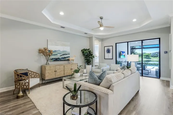 Living room with a tray ceiling, ornamental molding, wood-type flooring, and ceiling fan