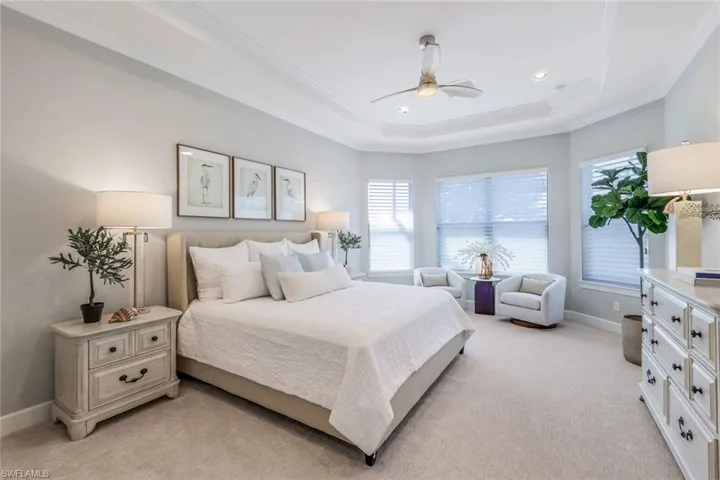 Bedroom with light carpet, ornamental molding, ceiling fan, and a raised ceiling