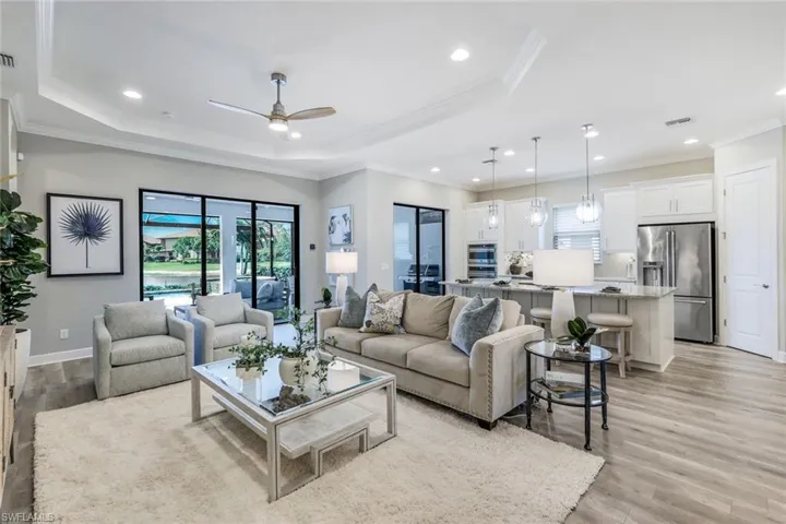 Living room featuring a raised ceiling, ceiling fan, and light wood-type flooring