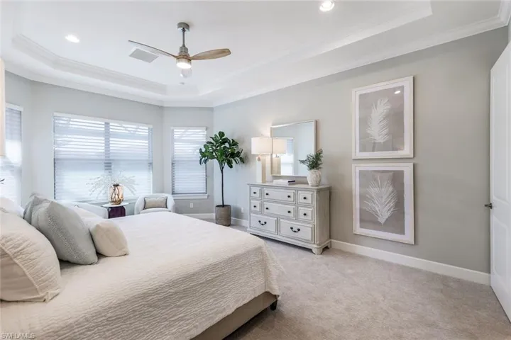 Carpeted bedroom featuring ornamental molding, ceiling fan, and a raised ceiling