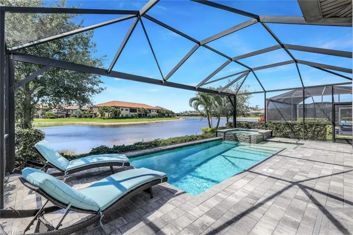 View of swimming pool featuring a patio area, glass enclosure, an in ground hot tub, and a water view