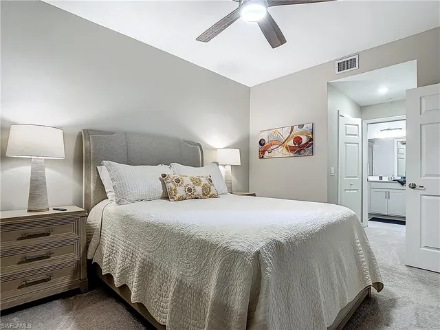 Carpeted bedroom featuring ensuite bath and ceiling fan