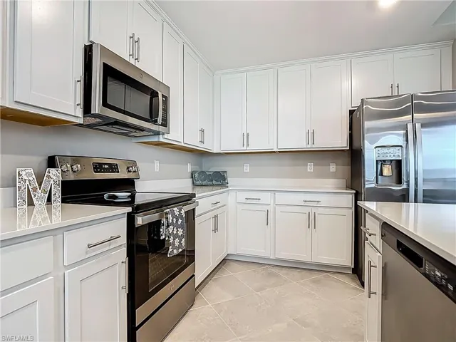 Kitchen with stainless steel appliances, light countertops, white cabinets, and light tile patterned floors