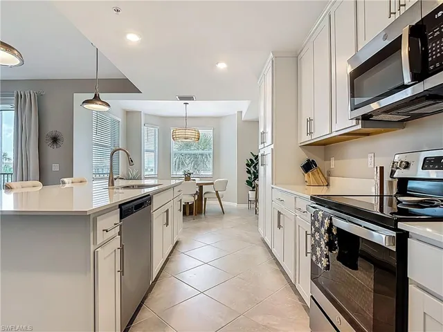 Kitchen with appliances with stainless steel finishes, light countertops, a center island with sink, decorative light fixtures, and recessed lighting