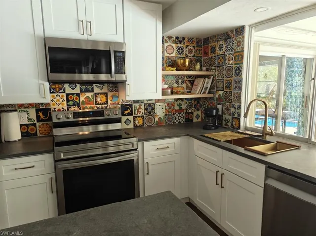 Kitchen with white cabinets, tasteful backsplash, appliances with stainless steel finishes, and sink