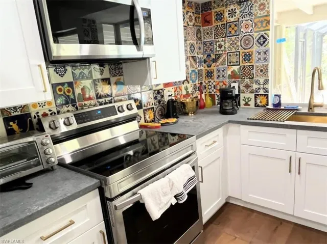 Kitchen with appliances with stainless steel finishes, white cabinets, and dark wood-type flooring