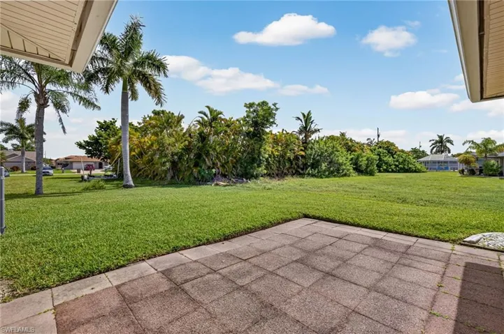 Spacious patio area featuring rectangular pavers and expansive green space with mature palm trees