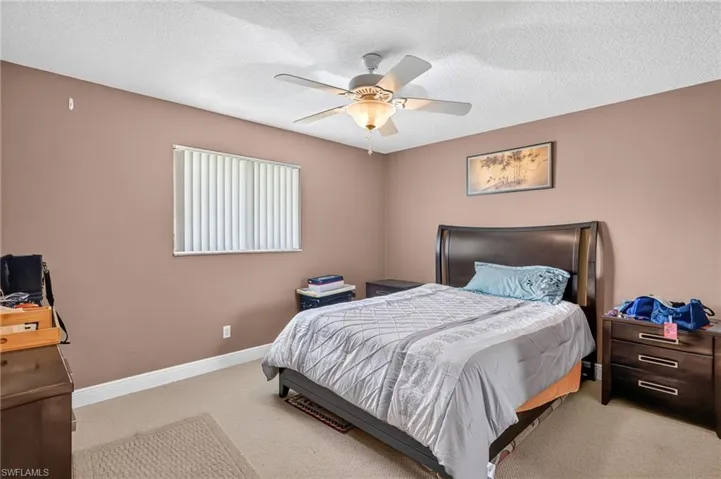 Soft neutral wall tones featuring a window with vertical blinds, light-colored carpet, a ceiling fan with integrated lighting, and white baseboards