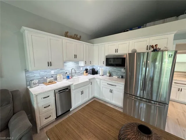 Kitchen with stainless steel appliances, white cabinets, sink, and lofted ceiling