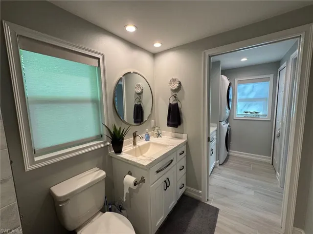Bathroom with stacked washer / drying machine, vanity, wood-type flooring, and toilet
