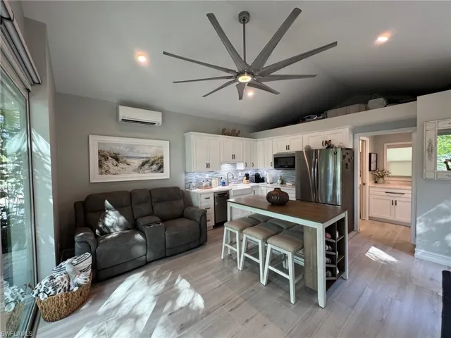 Kitchen with ceiling fan, a wall mounted AC, white cabinets, light wood-type flooring, and vaulted ceiling